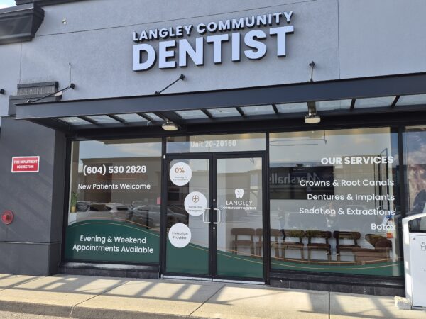 Storefront of Langley Community Dentist, featuring large windows displaying contact information and available services like crowns, root canals, dentures, and more.