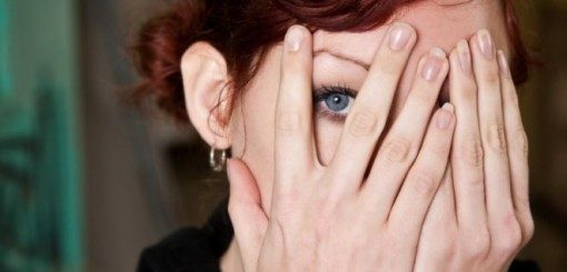 Woman peeking between fingers as she holds her hands in front of her face