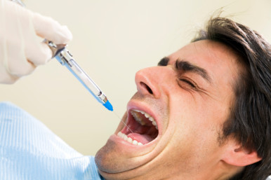 dentist holding a syringe and anesthetizing his terrified patient.