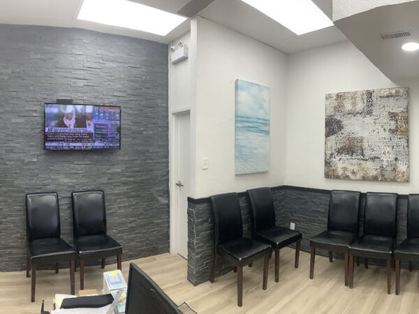 Dental office waiting room with black chairs, a wall-mounted TV, and two abstract paintings.