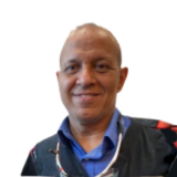 Smiling person in a blue shirt and dark jacket with a white background.