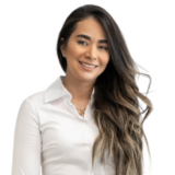 A woman with long, wavy hair smiles while wearing a white blouse against a plain background.