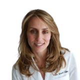 A smiling woman with long, light brown hair wearing a white coat, posing against a plain background.