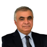 A confident man in a suit with a striped shirt and tie, posing against a plain white background.