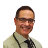 A smiling person wearing glasses, a light green checkered shirt, and a stethoscope around the neck, set against a plain white background.