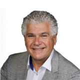 A smiling man with curly gray hair, wearing a gray checkered blazer and white shirt, against a white background.