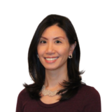 Smiling woman with dark hair, wearing a maroon top and a necklace, against a plain white background.
