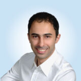 A person wearing a white shirt is smiling at the camera, set against a light blue background.