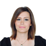 A woman with shoulder-length brown hair and a black top smiles softly against a plain white background.