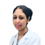 A person with dark hair tied back, wearing a white coat and smiling gently against a plain background.
