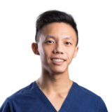 A young person in a blue medical scrub top is smiling against a plain white background.