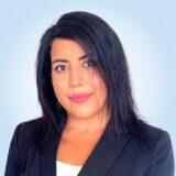 A professional-looking woman with long dark hair and a blazer smiles softly at the camera, set against a light blue background.