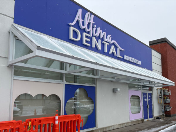Altima Dental clinic exterior with a blue and white color scheme, showcasing the business name prominently on the signage. Orange construction barriers are visible in front of the building.