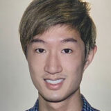 A person with short, light brown hair, wearing a checkered shirt, smiles warmly at the camera against a neutral background.