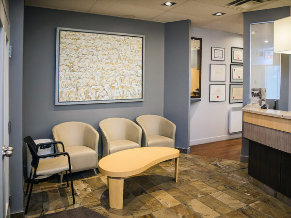 A warm dental office interior featuring comfortable seating, a coffee table, artwork on the walls, and a reception area. The atmosphere is inviting and relaxed, perfect for patients awaiting their appointments.