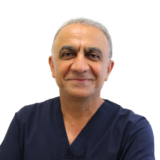 A smiling person in navy blue scrubs is standing against a white background.