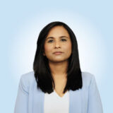 A professional woman with long black hair is wearing a light blue blazer and looking directly at the camera. The background is a soft blue gradient, creating a calming atmosphere.