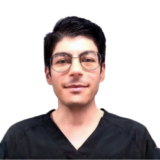 A person with short dark hair and glasses, wearing black scrubs, smiling at the camera against a plain white background.