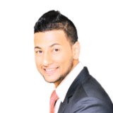 A smiling man in a suit with dark hair and a red tie, facing forward against a white background.