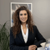 A friendly woman with curly hair, wearing a blazer, stands beside a fishbowl in an inviting office environment.