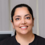 A smiling dental professional wearing a black shirt is pictured, exuding warmth and approachability in a clinical environment.