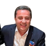 Smiling man in a dark suit with a colorful pocket square, on a plain white background.