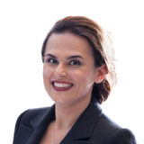 A smiling individual with dark hair is wearing a black blazer against a plain white background.