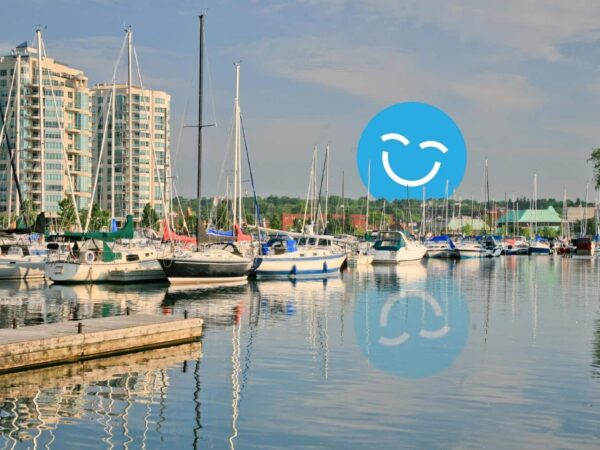 A serene marina scene featuring multiple sailboats docked in calm waters, with modern buildings in the background and a cheerful smiley face overlaid in blue.
