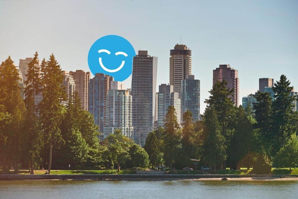 A city skyline with tall skyscrapers and lush green trees by a calm water body, featuring a large blue smiling face in the sky.
