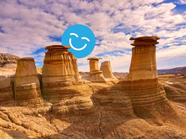Rock formations, known as hoodoos, in a desert landscape under a partly cloudy sky with a smiling emoji in the foreground.