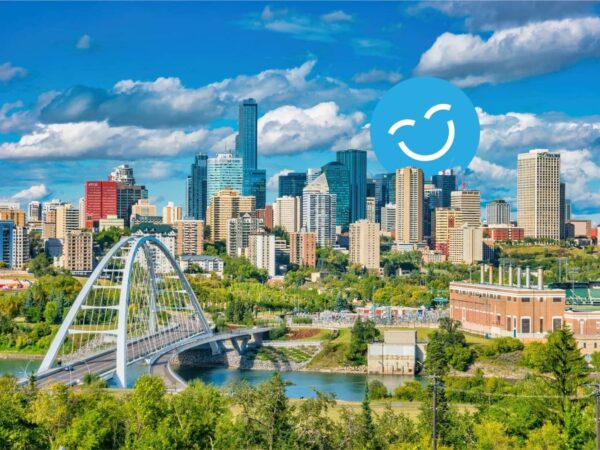 City skyline with modern skyscrapers, a white bridge, and lush greenery under a blue sky with clouds and a smiling face icon.