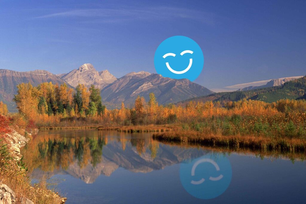 A serene landscape featuring vibrant autumn foliage along a calm river, with majestic mountains in the background. A friendly blue smiley face, the 123Dentist Smiley, adds a cheerful touch to the scene.