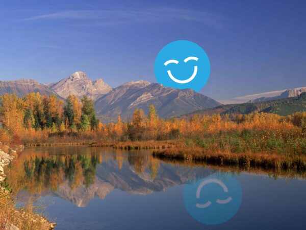 A serene landscape featuring vibrant autumn foliage along a calm river, with majestic mountains in the background. A friendly blue smiley face, the 123Dentist Smiley, adds a cheerful touch to the scene.