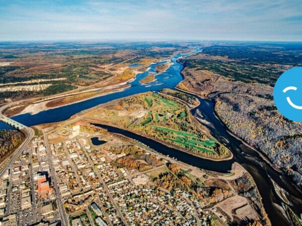 Aerial view of a landscape featuring winding rivers, lush greenery, and a small town adjacent to the water. The scene highlights the natural beauty of the area, with rolling hills and a clear blue sky in the background.