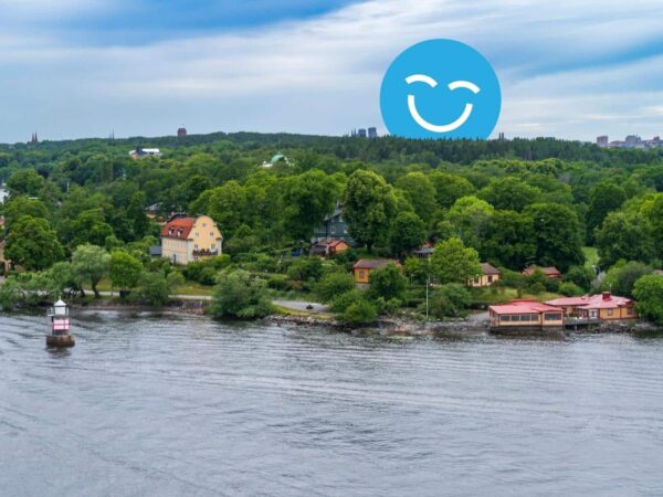 A serene waterscape features a lush green shoreline dotted with colorful homes. A small boat glides along the calm water under a cloudy sky, while a blue smiley face icon adds a cheerful element to the scene.
