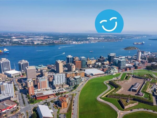 Aerial view of a vibrant cityscape by the waterfront, featuring tall buildings and green spaces. In the sky, a blue smiley face icon adds a cheerful touch to the scene, capturing a lively urban atmosphere.