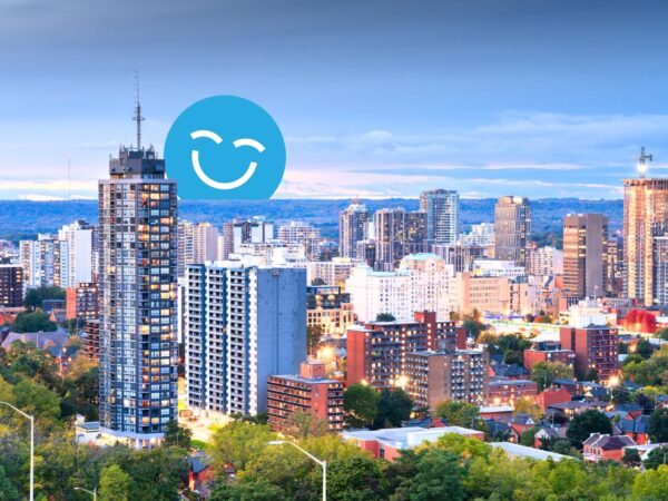A city skyline at dusk featuring modern buildings, with a blue smiley face graphic overlay. The scene reflects a blend of urban architecture and natural greenery, conveying a vibrant and lively atmosphere.