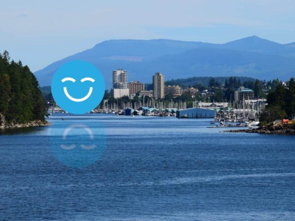 A scenic view of a calm river with lush trees on either side, leading to a city skyline in the background, framed by mountains. A large blue smiley face overlays the image, adding a cheerful element to the landscape.