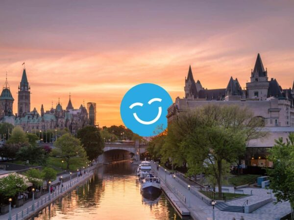 A scenic view of a city at sunset, featuring historical buildings along a river, with trees and boats in the foreground. A blue smiling face icon is superimposed at the center.