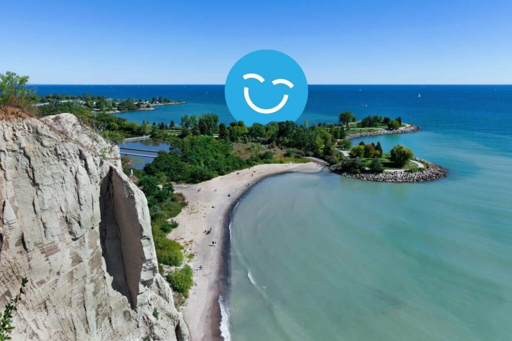 Une vue pittoresque d'une plage de sable et d'eaux turquoise entourées de verdure luxuriante, avec un ciel bleu éclatant au-dessus et une icône de visage souriant superposée sur l'image.