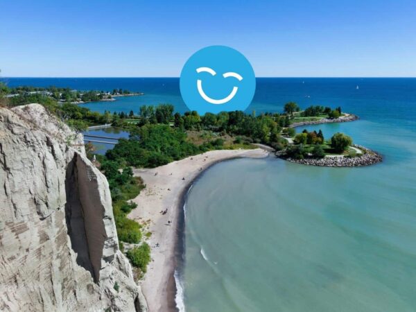 A scenic view of a sandy beach and turquoise waters surrounded by lush greenery, with a bright blue sky overhead and a smiling face icon superimposed on the image.