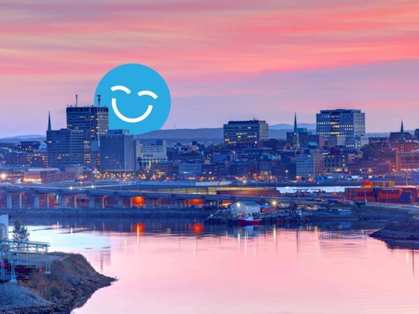A serene city skyline at sunset, reflecting in the water below. A large blue smiley face overlays the scene, adding a cheerful element to the tranquil atmosphere.