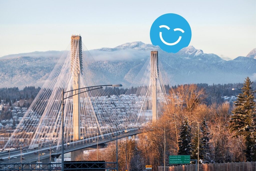 A view of a suspension bridge with mountains in the background, surrounded by trees. A blue smiling face is superimposed in the sky above the bridge.