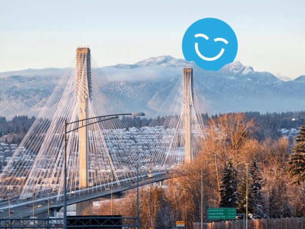 A view of a suspension bridge with mountains in the background, surrounded by trees. A blue smiling face is superimposed in the sky above the bridge.