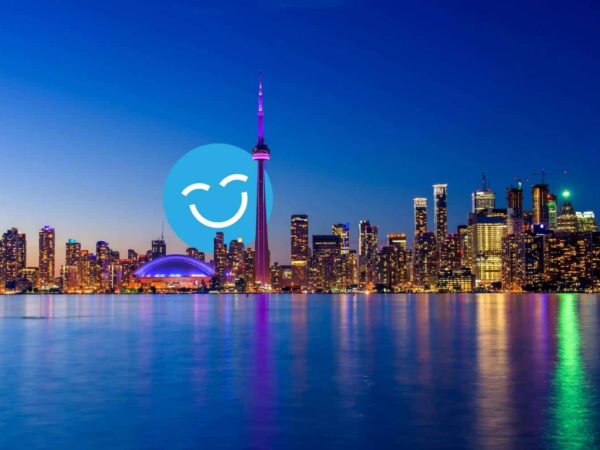 Toronto skyline at dusk, featuring illuminated skyscrapers and the CN Tower reflecting on Lake Ontario. A smiley face icon overlays part of the scene.