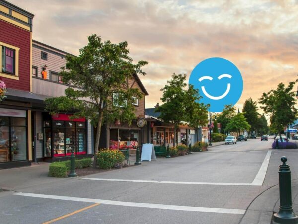 A quiet, tree-lined street with small shops under a sunset sky, featuring a superimposed blue smiley face in the sky.