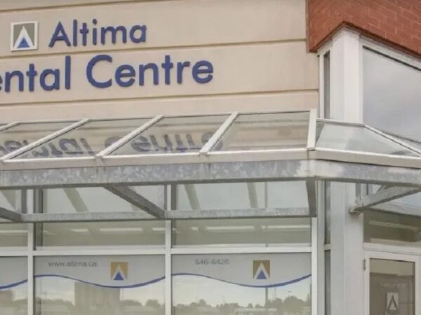 The image shows the exterior of the Altima Dental Centre, featuring a modern glass entrance with a canopy and signage displaying the name of the dental practice. The building has a brick facade, contributing to a professional and welcoming appearance.