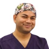 A smiling healthcare professional wearing a colorful surgical cap and purple scrubs.