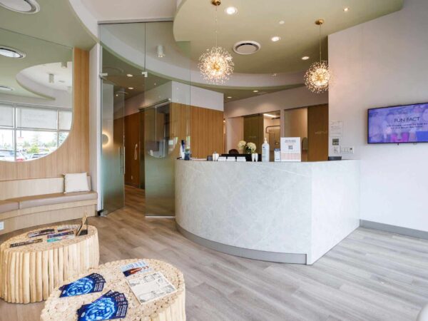A modern reception area features a curved front desk, stylish seating, and warm wood accents. Soft lighting and a contemporary design create a welcoming atmosphere. A flat-screen TV is mounted on the wall, and decorative elements add a touch of elegance.