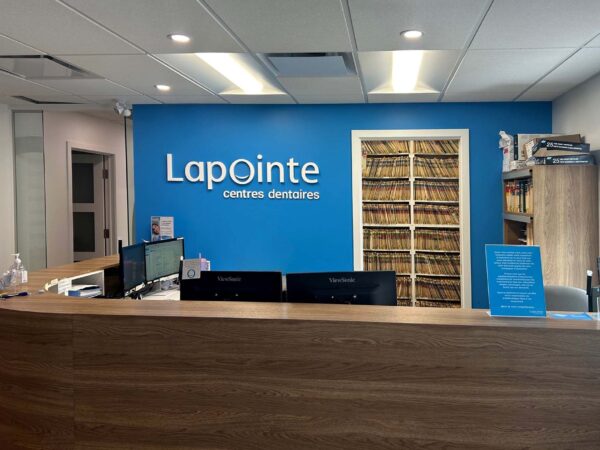 A modern dental office reception area featuring a wooden desk, blue walls with the name "Lapointe" prominently displayed, and shelves lined with patient files. The space is well-lit and organized, creating a welcoming atmosphere for visitors.